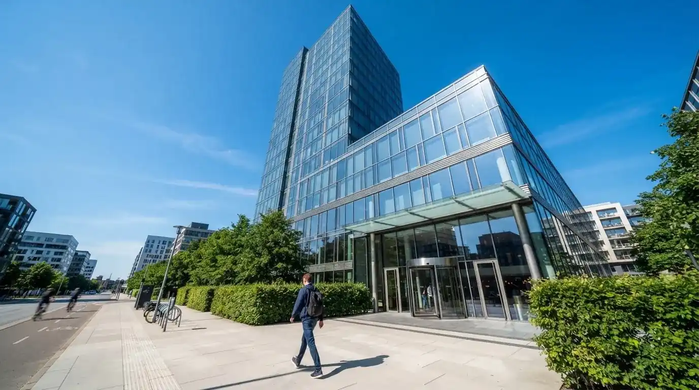 En moderne glasbygning i Ørestad en lys dag med en fodgænger i forgrunden og blå himmel bag facaden.